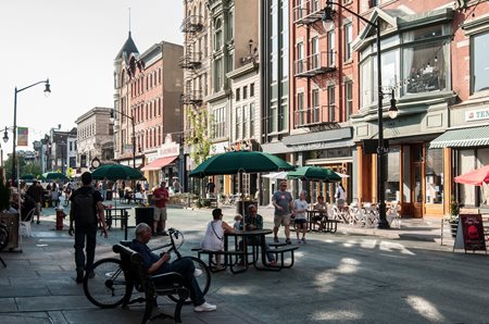 People sit at tables in pedestrian plaza which used to be a through street for cars