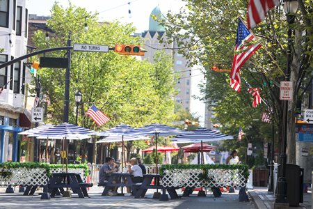 People dine at picnic tables in the street within barricades to protect from traffic