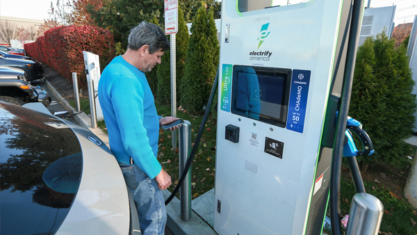 Man accesses phone app to charge vehicle at electric charging station